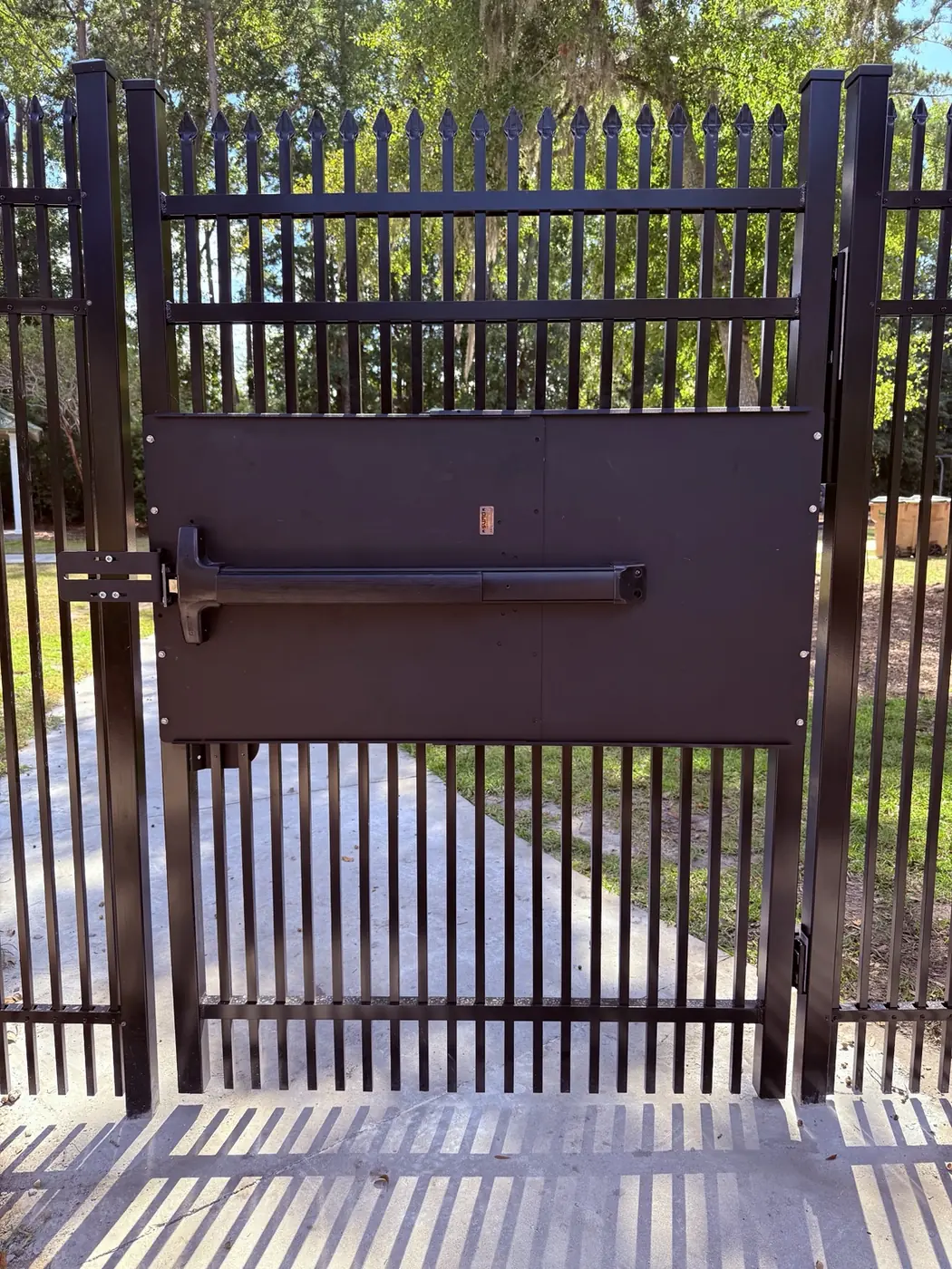Push-bar exit hardware installed on a black aluminum gate at the Buckhead East pool