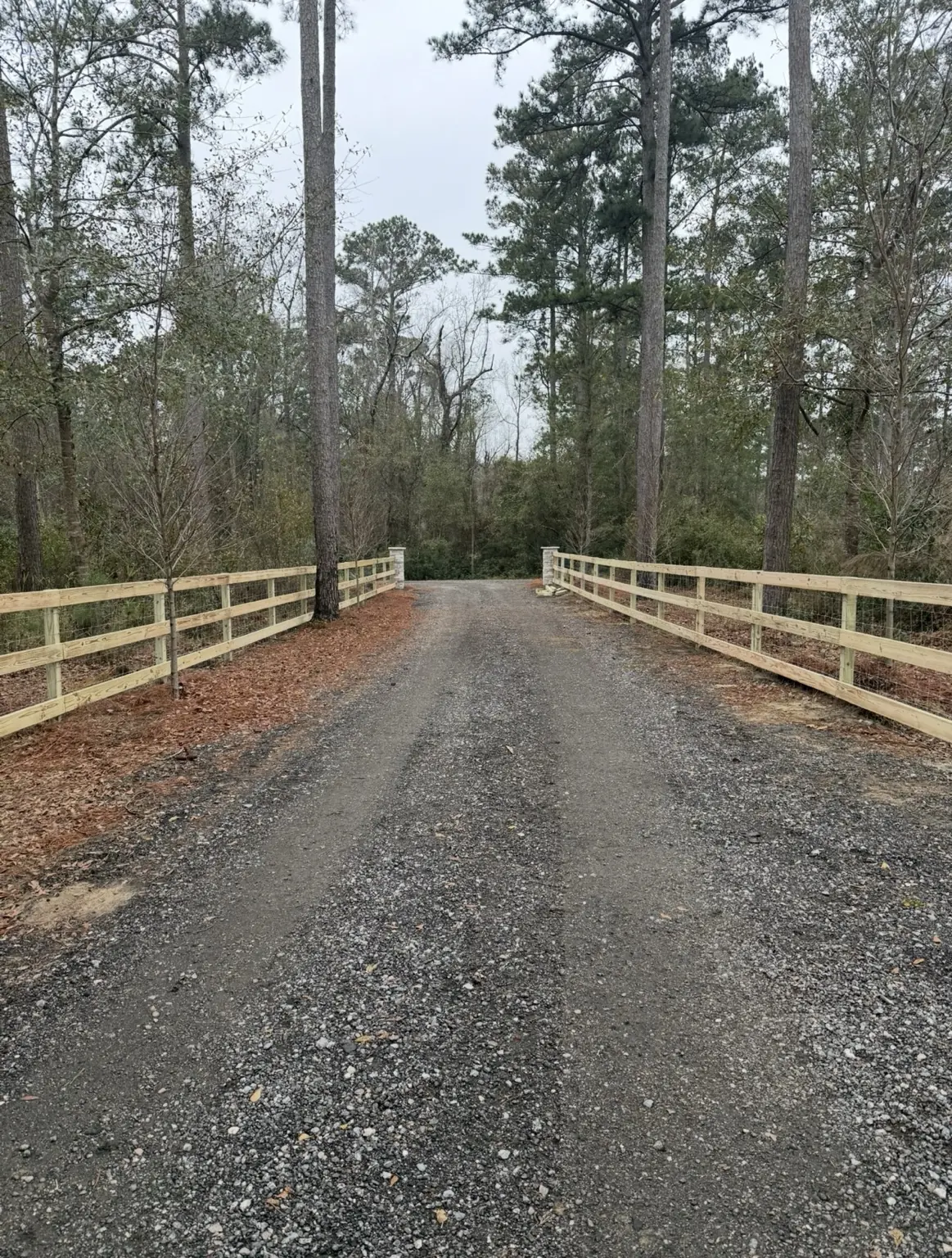 Wood and wire farm fencing lining a gravel property entrance