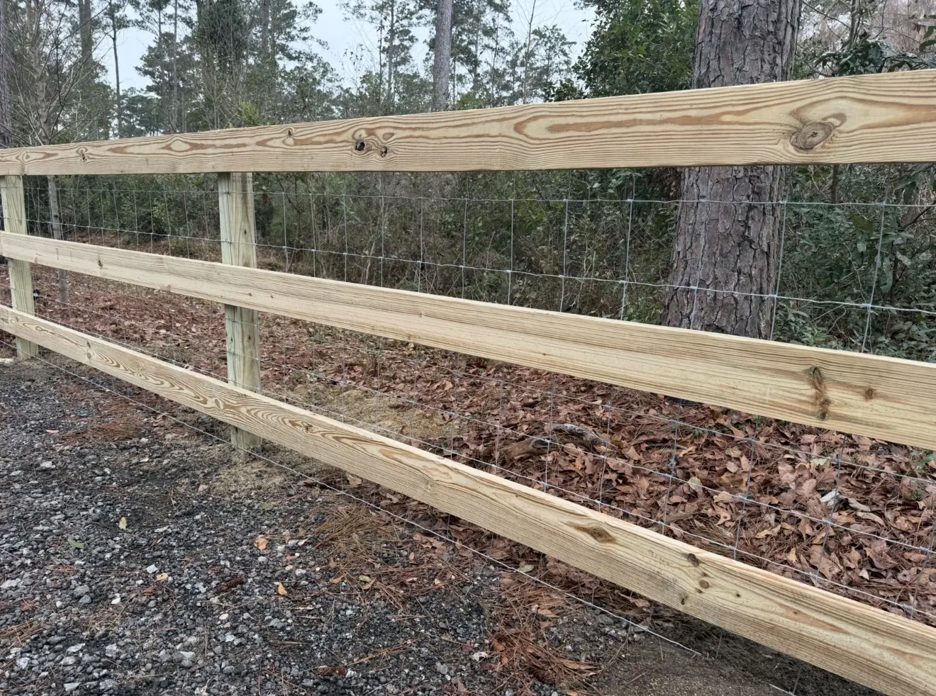 Three-rail wood farm fence with wire mesh