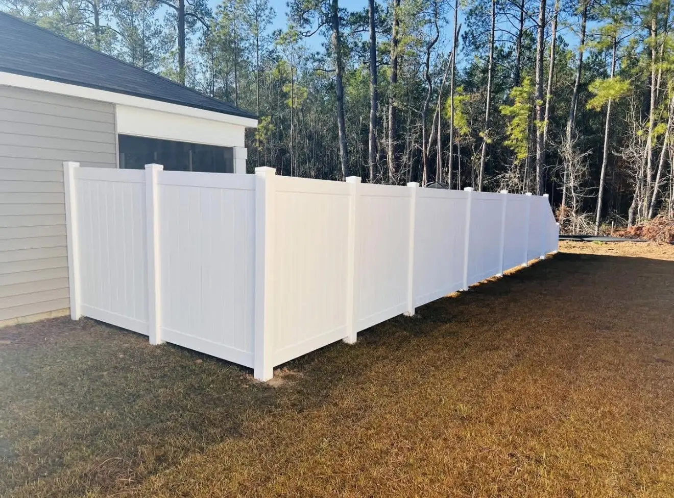 White vinyl privacy fence enclosing a backyard beside a gray home