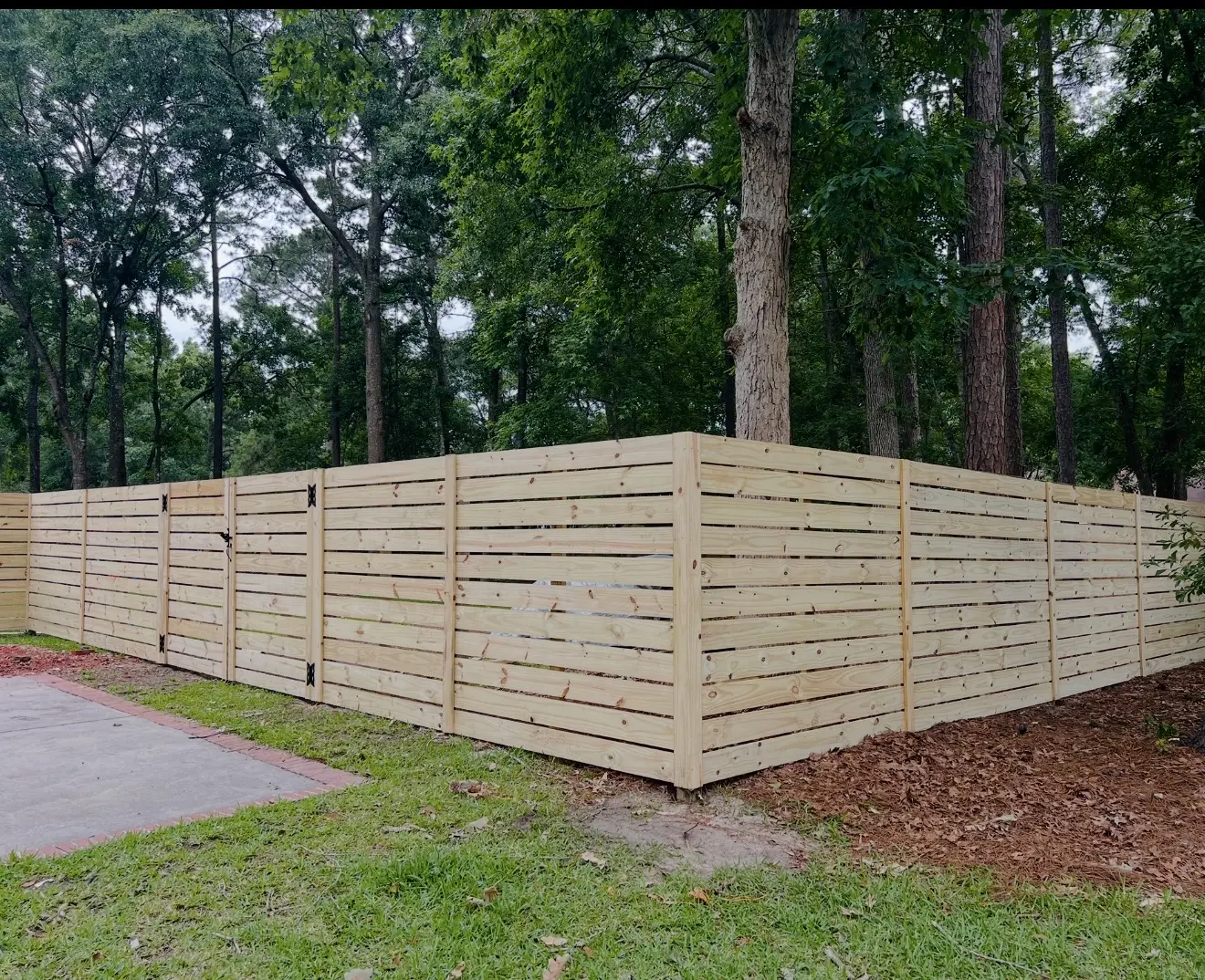 Long horizontal pressure-treated wood privacy fence along a wooded residential yard