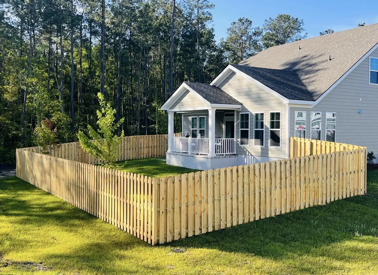 Pressure-treated shadowbox fence surrounding a gray home beside a wooded property
