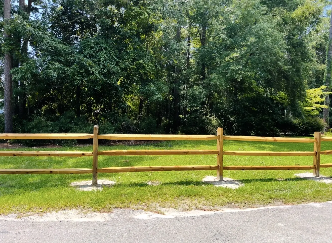 Three-rail split-rail fence along a grassy roadside property line